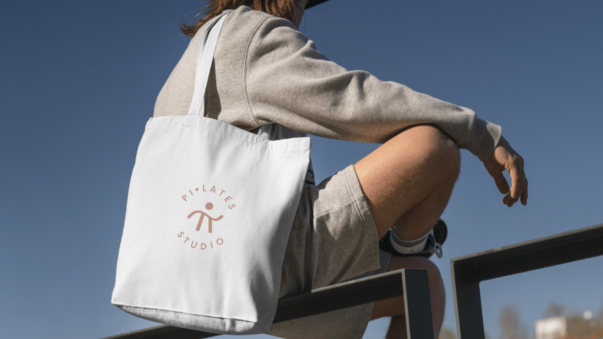Mockup de una tote bag blanca de tela con el logotipo de Pi-lates Studio impreso en tono salmón. Diseño de aplicaciones físicas y branding creado por Outroute Digital.
